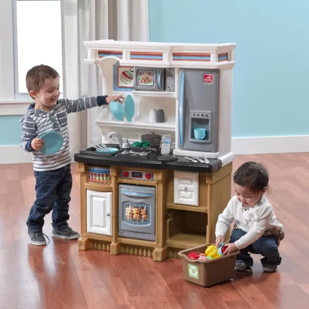 Kids playing with a realistic pretend play kitchen set featuring toy fridge, oven, and cookware