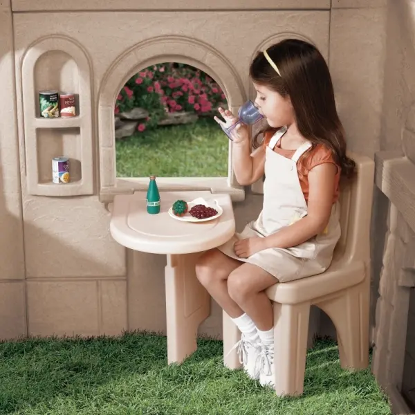 Kids playing with a realistic outdoor cottage playhouse featuring red door, green shutters, and stone design