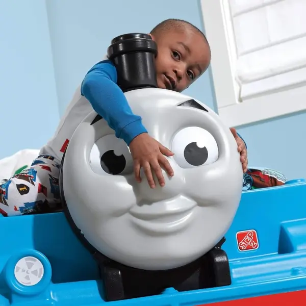Toddler boy reading in a blue Thomas the Tank Engine-themed bed with smiling front design at Butterflies Toys, HSR Layout, Bengaluru.